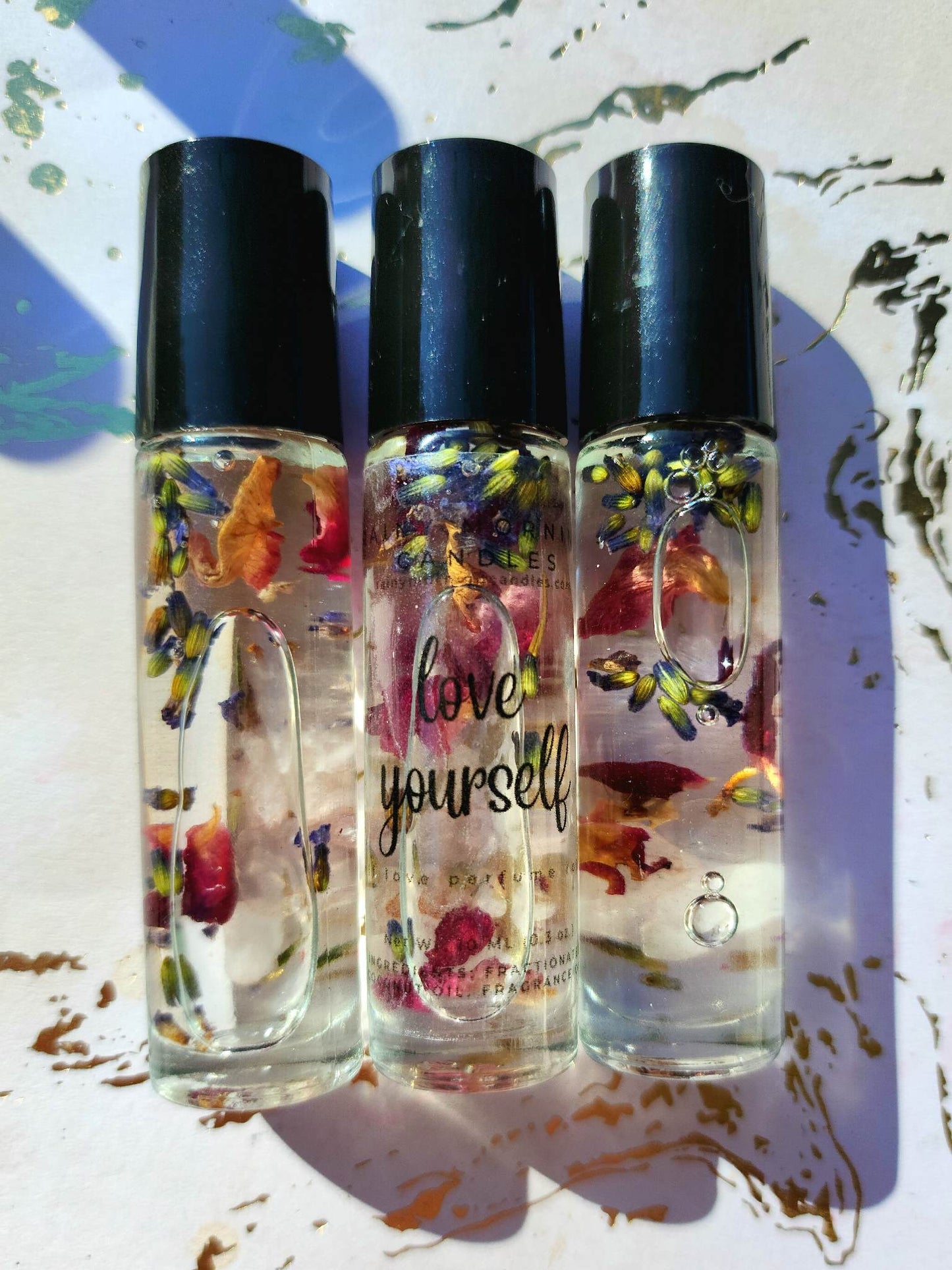 glass roller ball perfume bottles with black caps laying on white and gold background. the label on the bottle reads love yourself